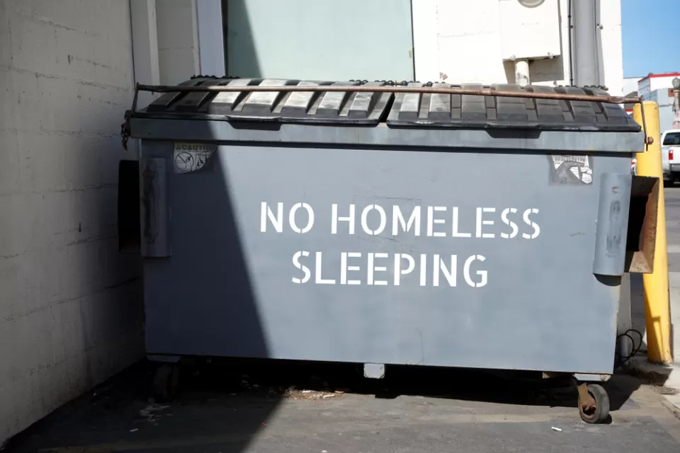 "No homeless sleeping" stenciled on grey dumpster in urban alley